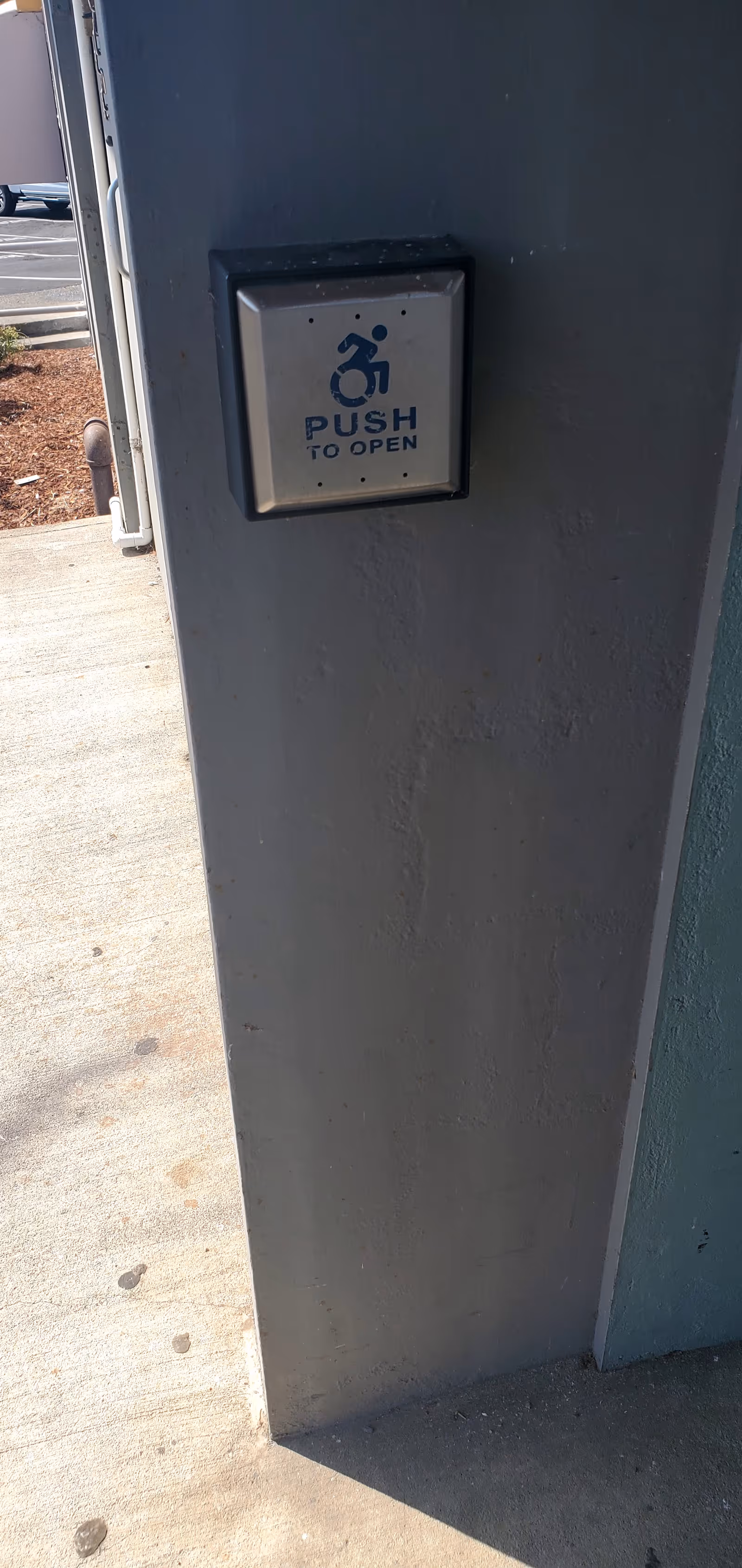 Exterior wall with a wheelchair-accessible push-to-open button beside a doorway.