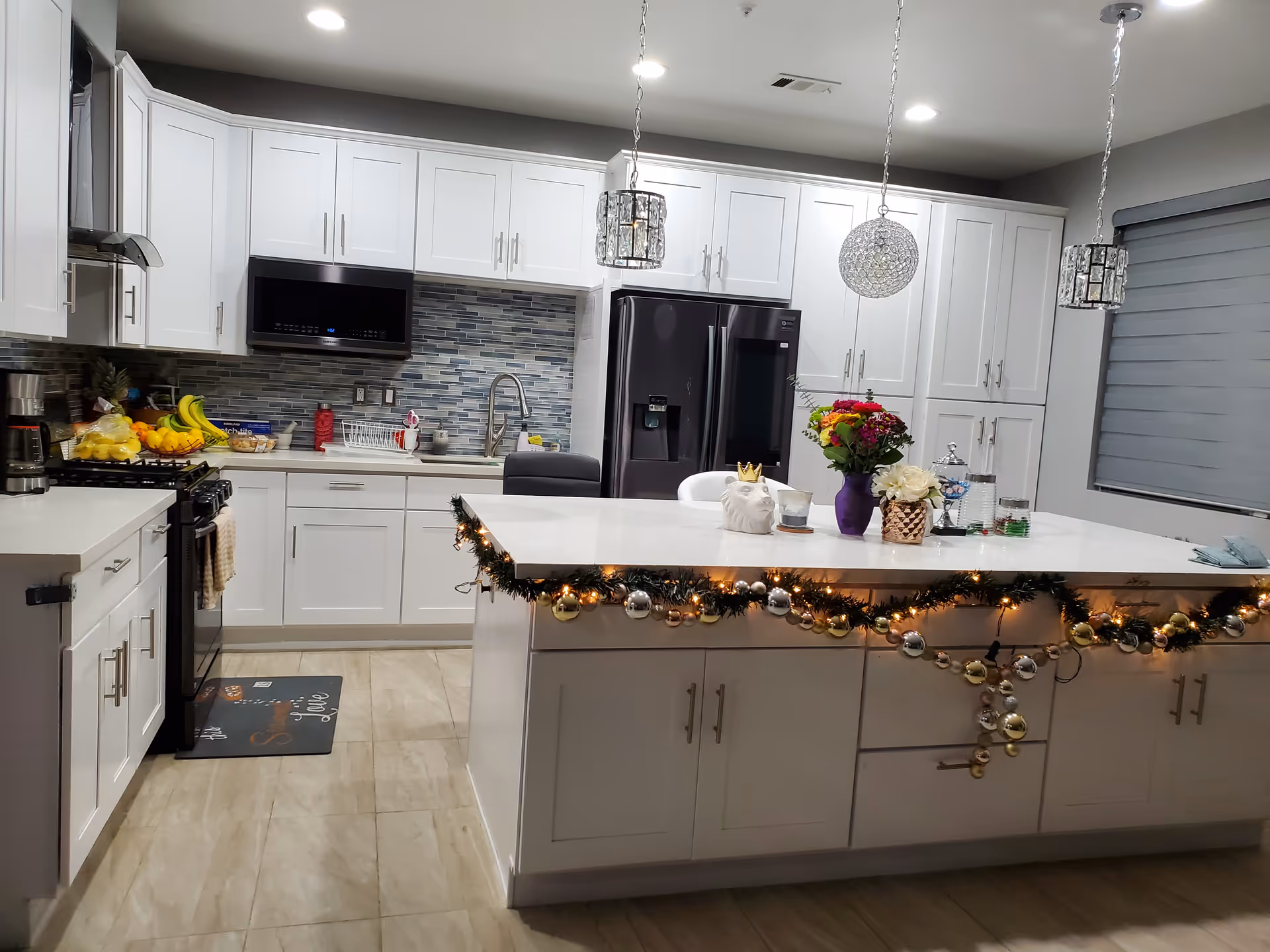 White kitchen with island, festive garland, and flowers near stainless appliances.