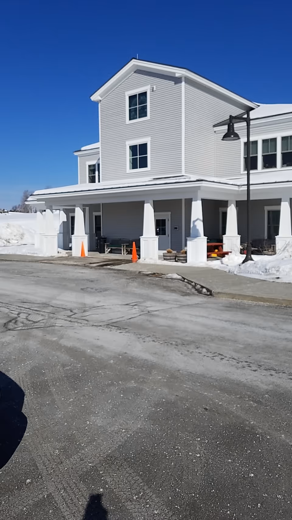 White two-story senior living building with a covered entrance, snow, and orange traffic cones.