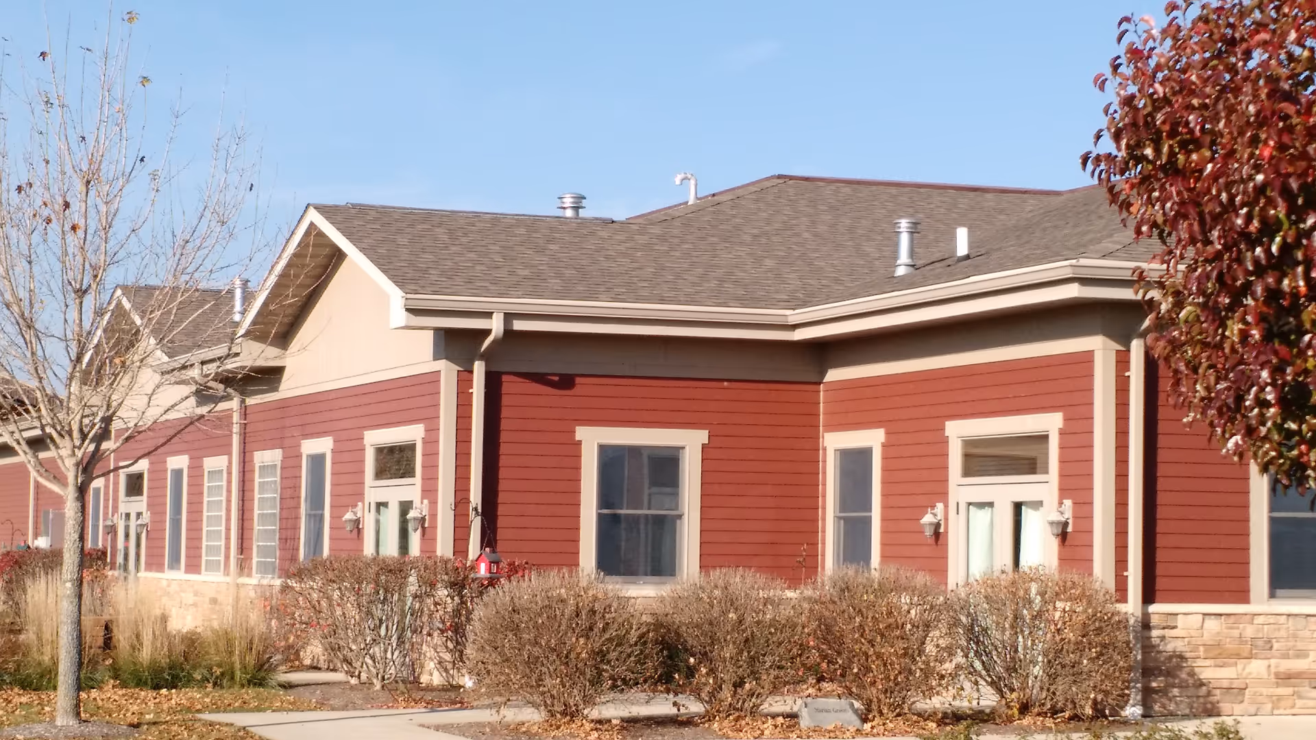 Red suburban senior living facility exterior with windows, shrubs, and a clear blue sky.