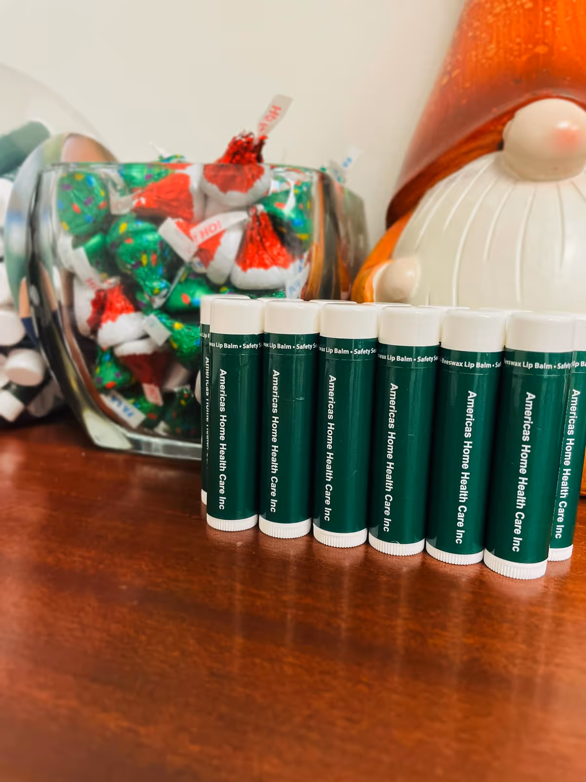 Row of green lip balm tubes labeled America's Home Health Care Inc on a wooden table
