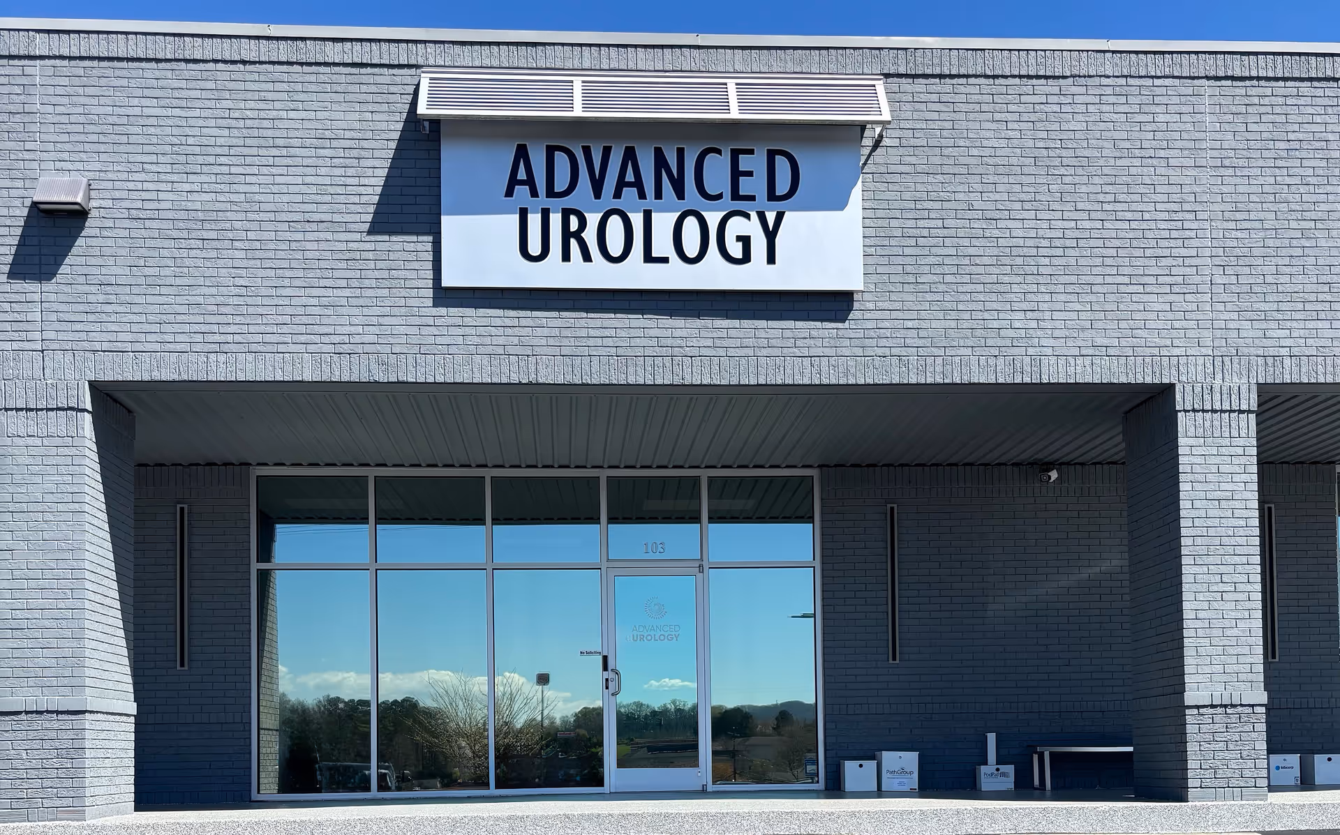 Front view of a gray brick medical building with glass doors and an Advanced Urology sign.