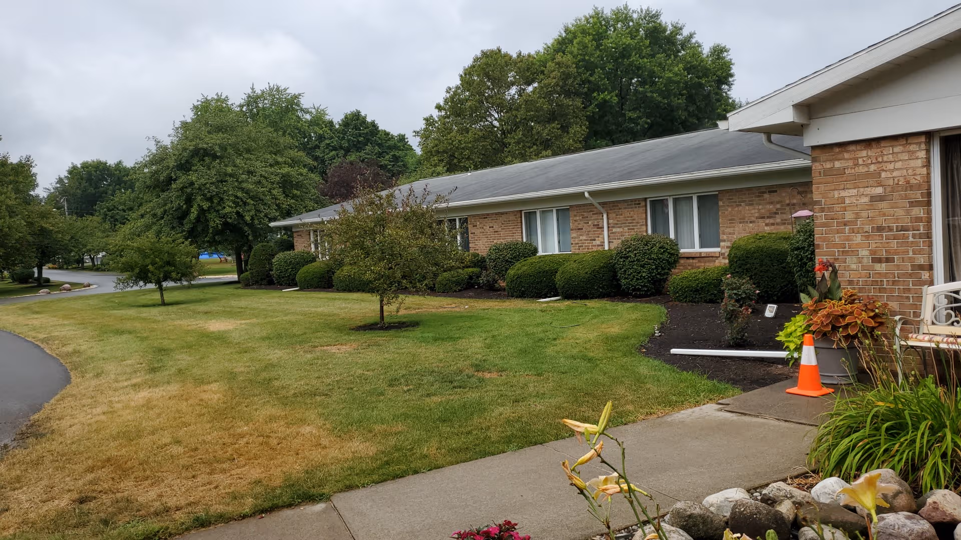 The Village at Penfield exterior: brick building, manicured lawn, trees, and walkway.
