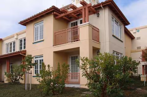 Two-story beige senior facility exterior with balconies and landscaped yard.
