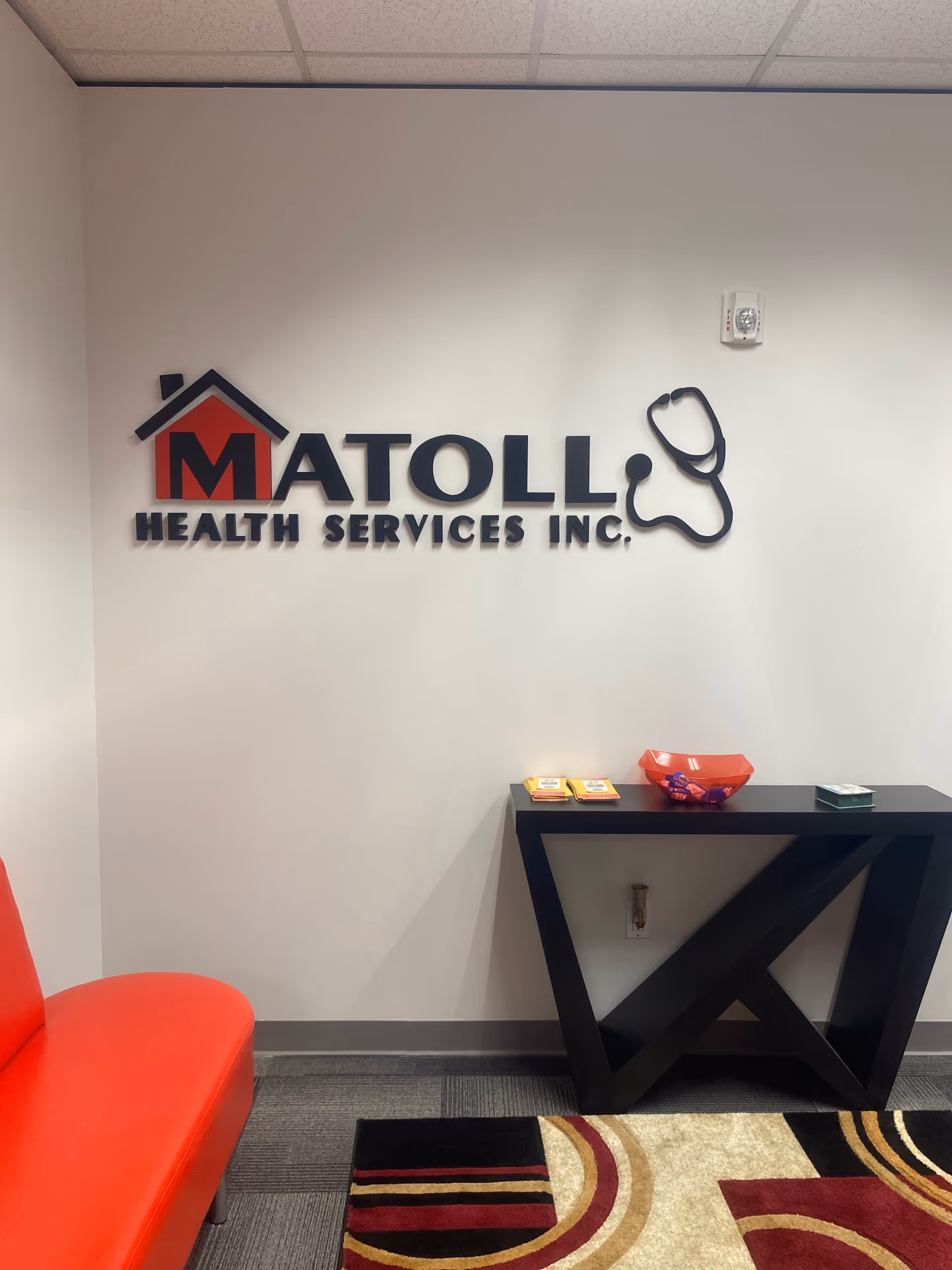 Interior hallway with Matoll Health Services Inc logo on the wall and a black console table.
