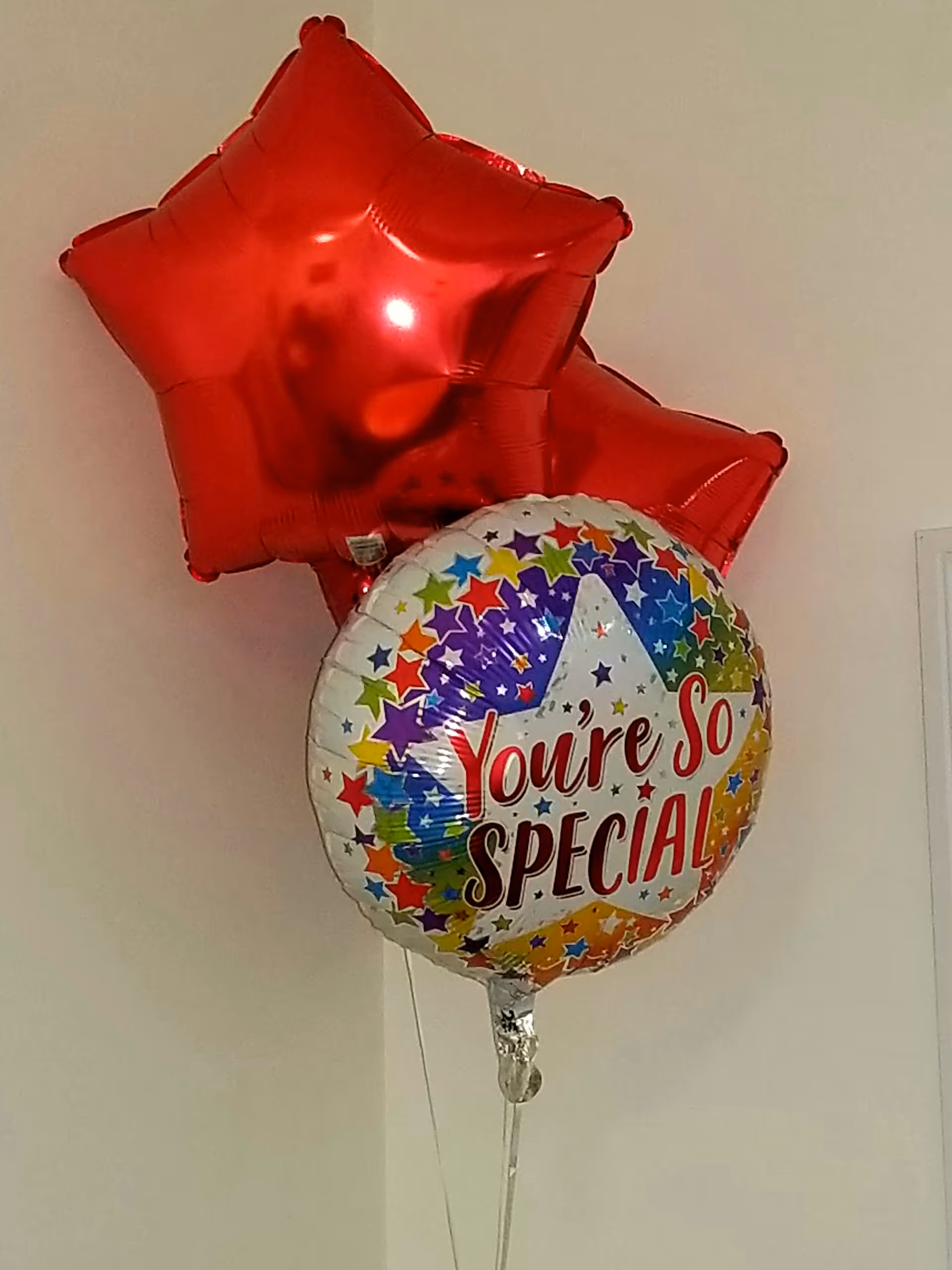 Colorful balloons indoors, including a round You're So Special balloon near a plain wall.