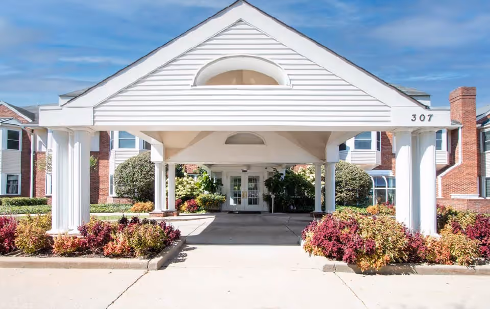 Front entrance of a senior living facility with a covered driveway and landscaped shrubs.