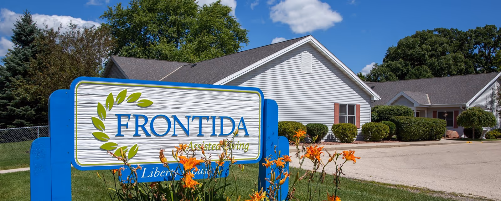 Blue Frontida Assisted Living sign in front of a light-colored building on a sunny day.