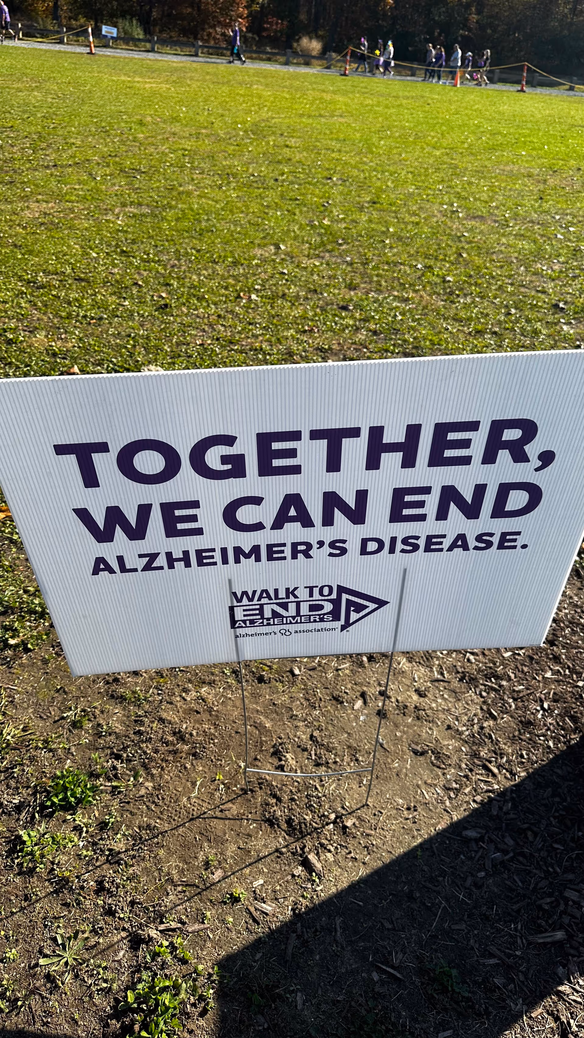 Outdoor Walk to End Alzheimer's sign on grass, with distant walkers in the background.
