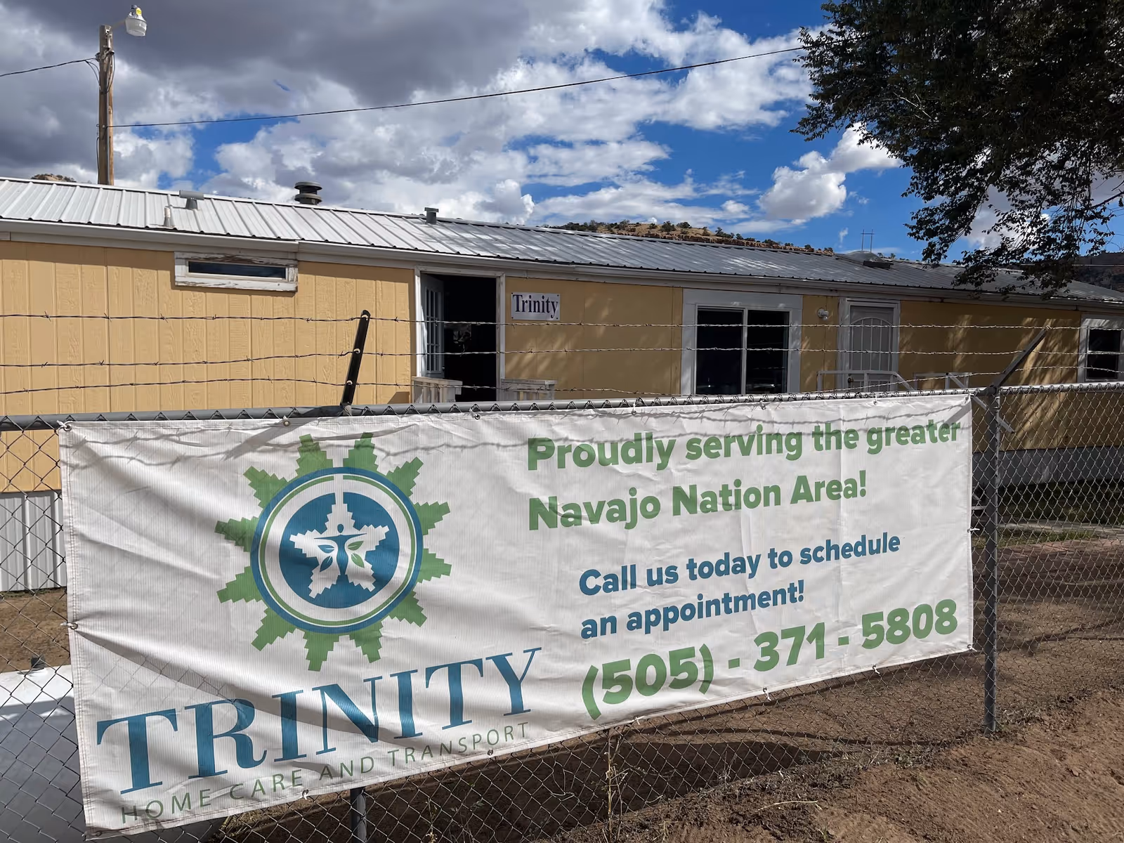 Exterior of a tan building behind a fence with a Trinity Home Care & Transport banner.