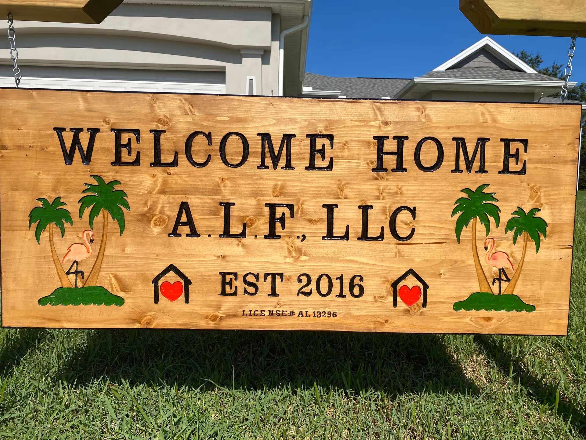 Wooden sign reading Welcome Home ALF LLC with palm trees on a grassy lawn
