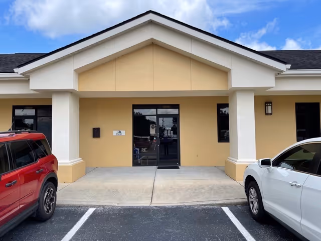 Front view of a beige senior living facility entrance with columns and parked cars.