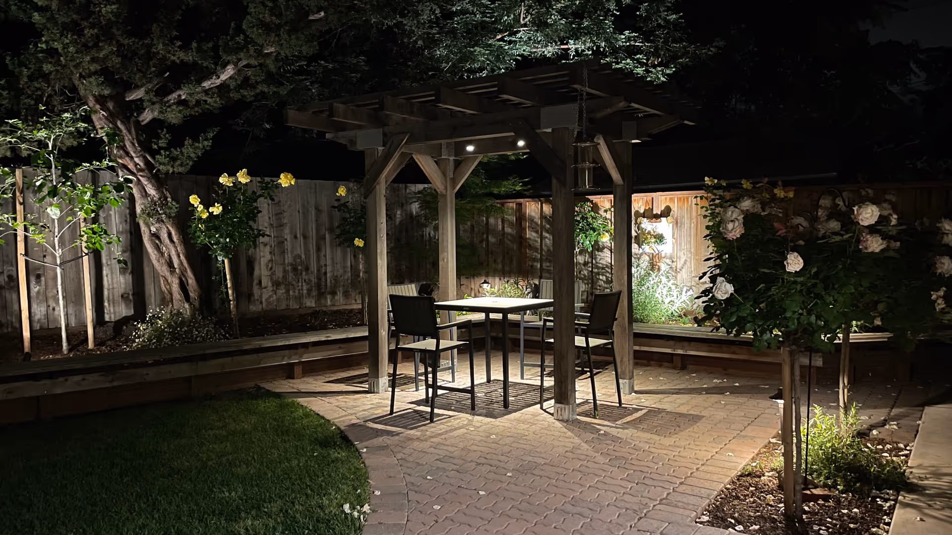 Outdoor patio at Maryland Home with a wooden pergola, table, chairs, and blooming roses.
