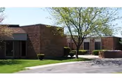 Brick exterior of a senior care facility with a tree-lined walkway and manicured lawn.