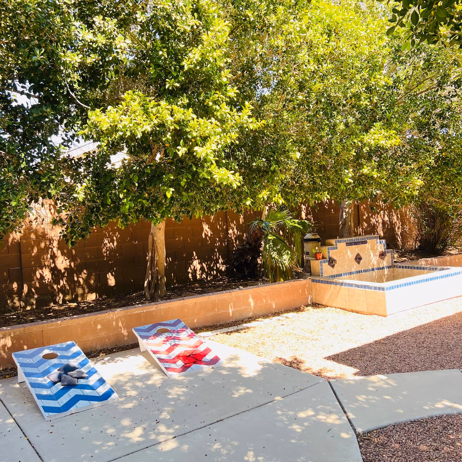 Shaded outdoor courtyard with striped lounge chairs, a tiled fountain, and a brick wall.