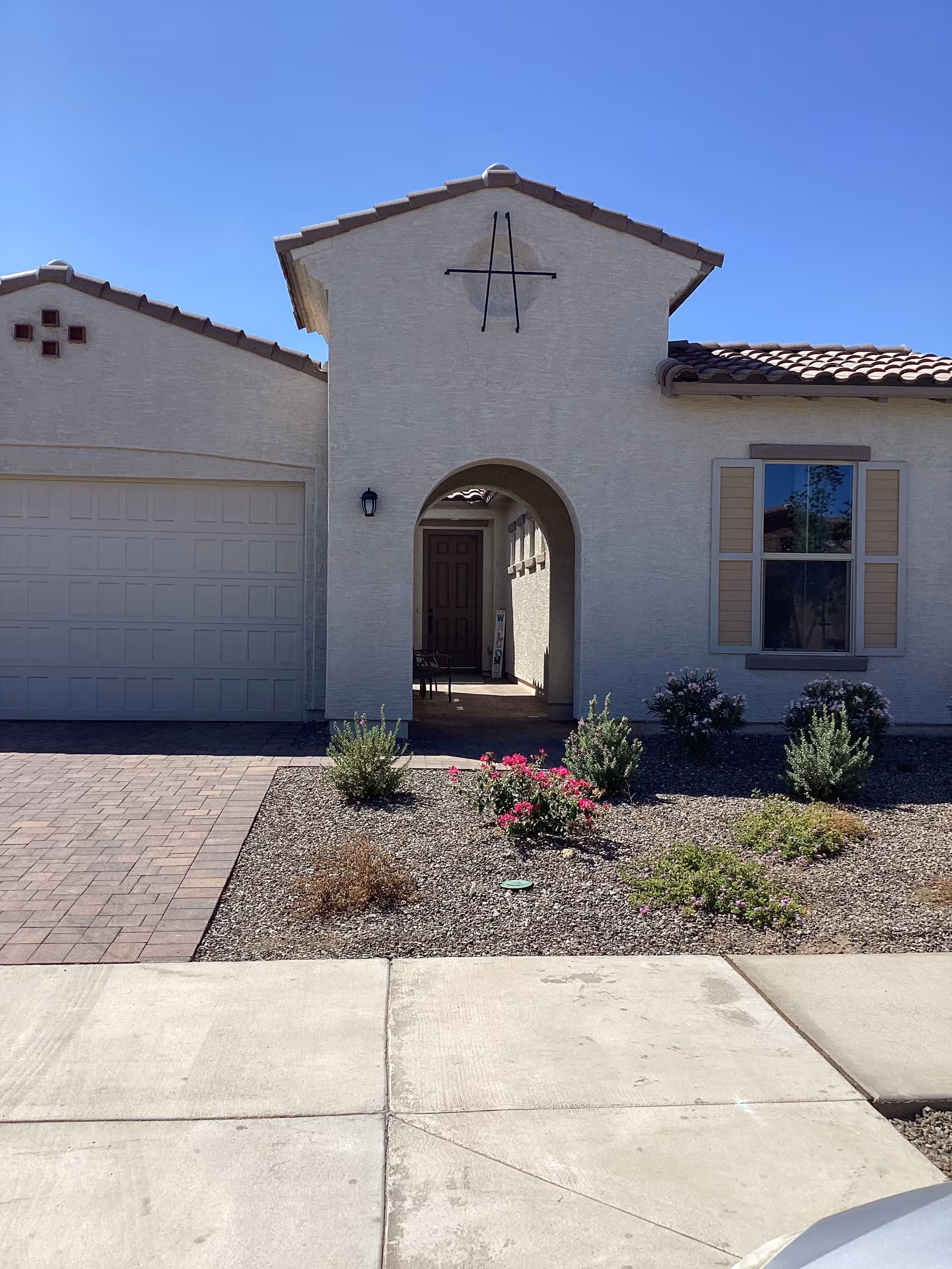 Front view of a beige senior living facility with an arched entry, garage, and desert landscaping.