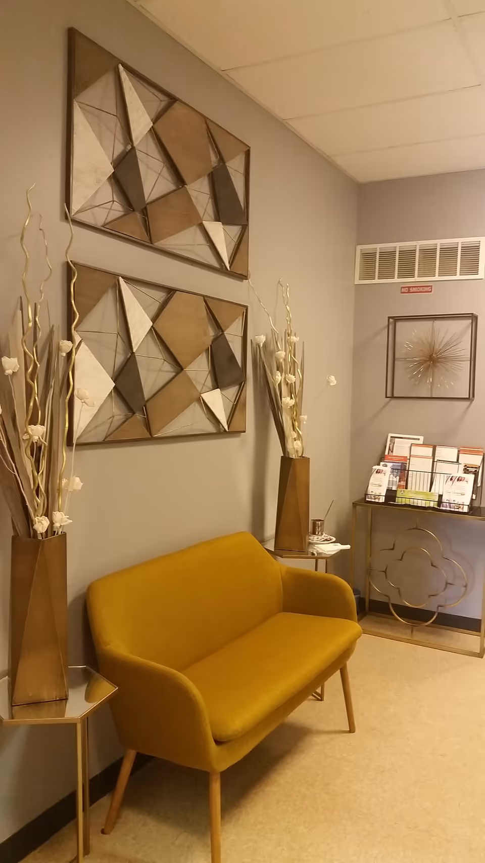 A mustard-yellow sofa sits in a modern waiting area with abstract wall art and brochures.