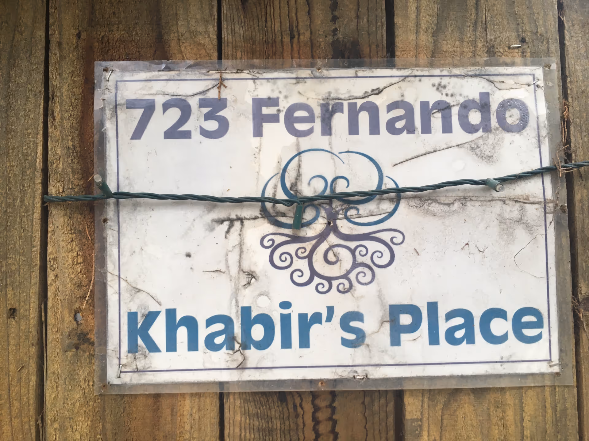 Weathered sign on wooden boards reading '723 Fernando' and 'Khabir's Place'.