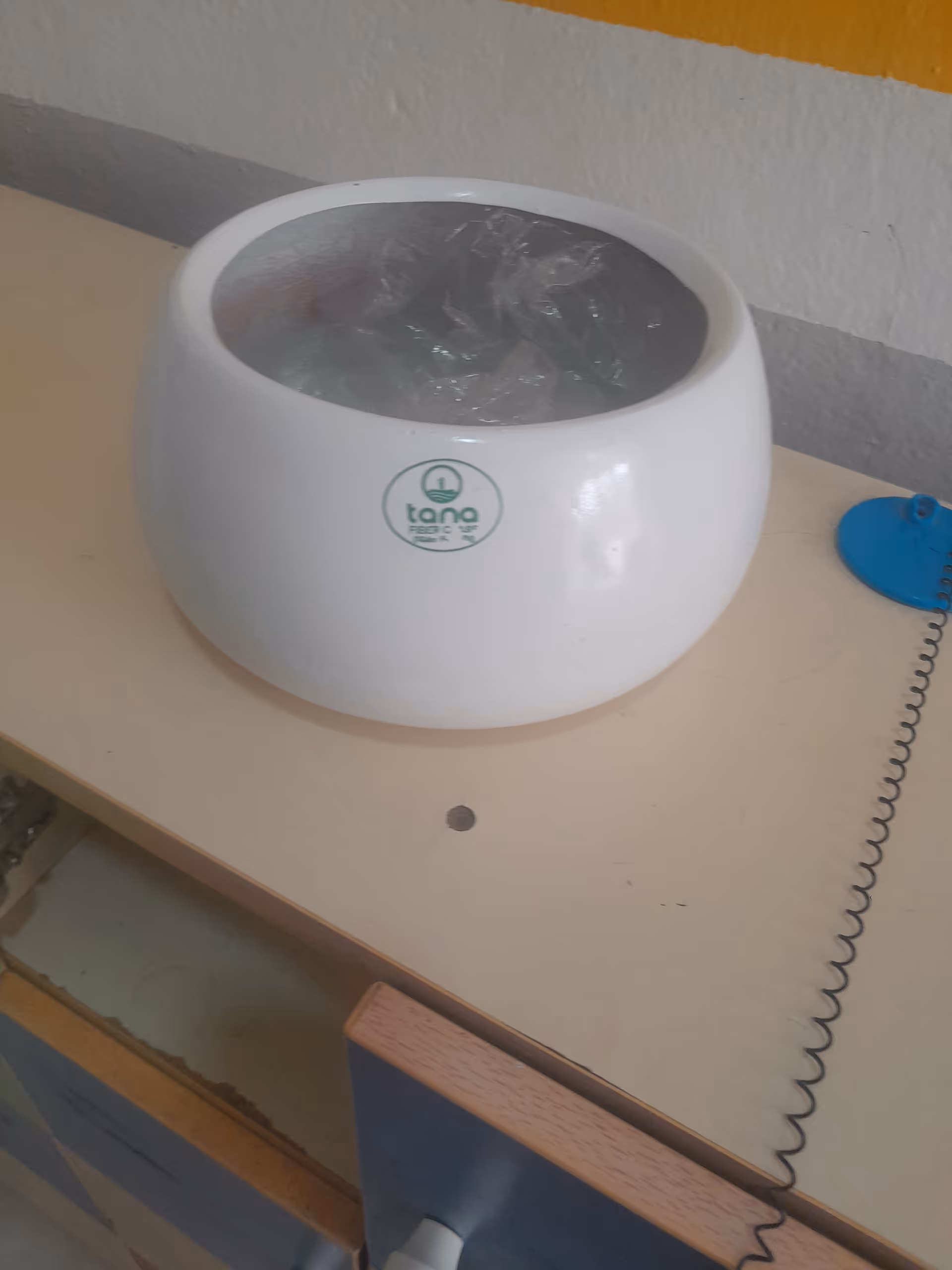 White round ceramic bowl sits on a beige desk with a coiled cord nearby.