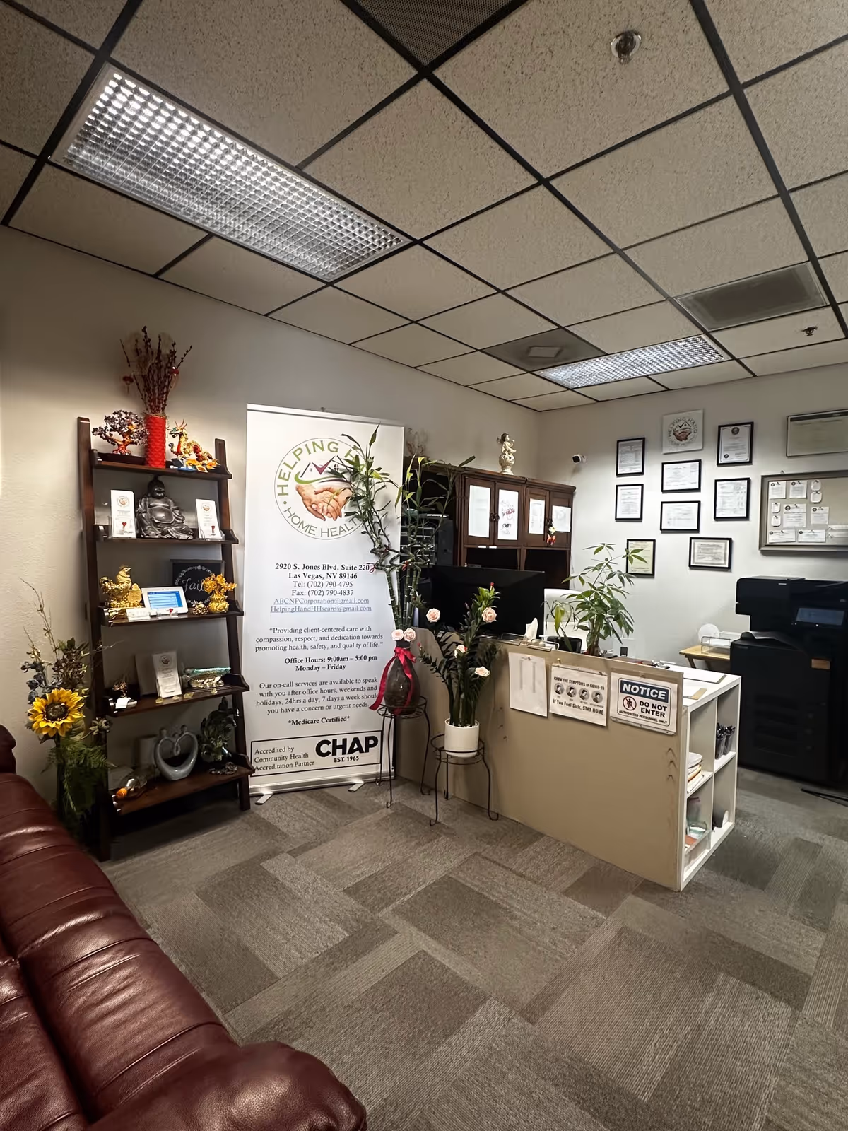 Reception area with banner, desk, shelves, plants, and framed certificates.
