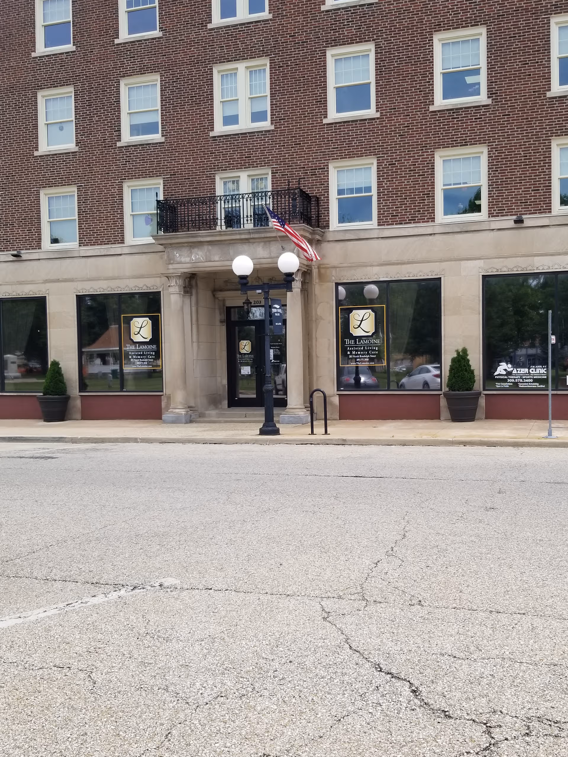 Brick building exterior with a central entrance, American flag, and signage.