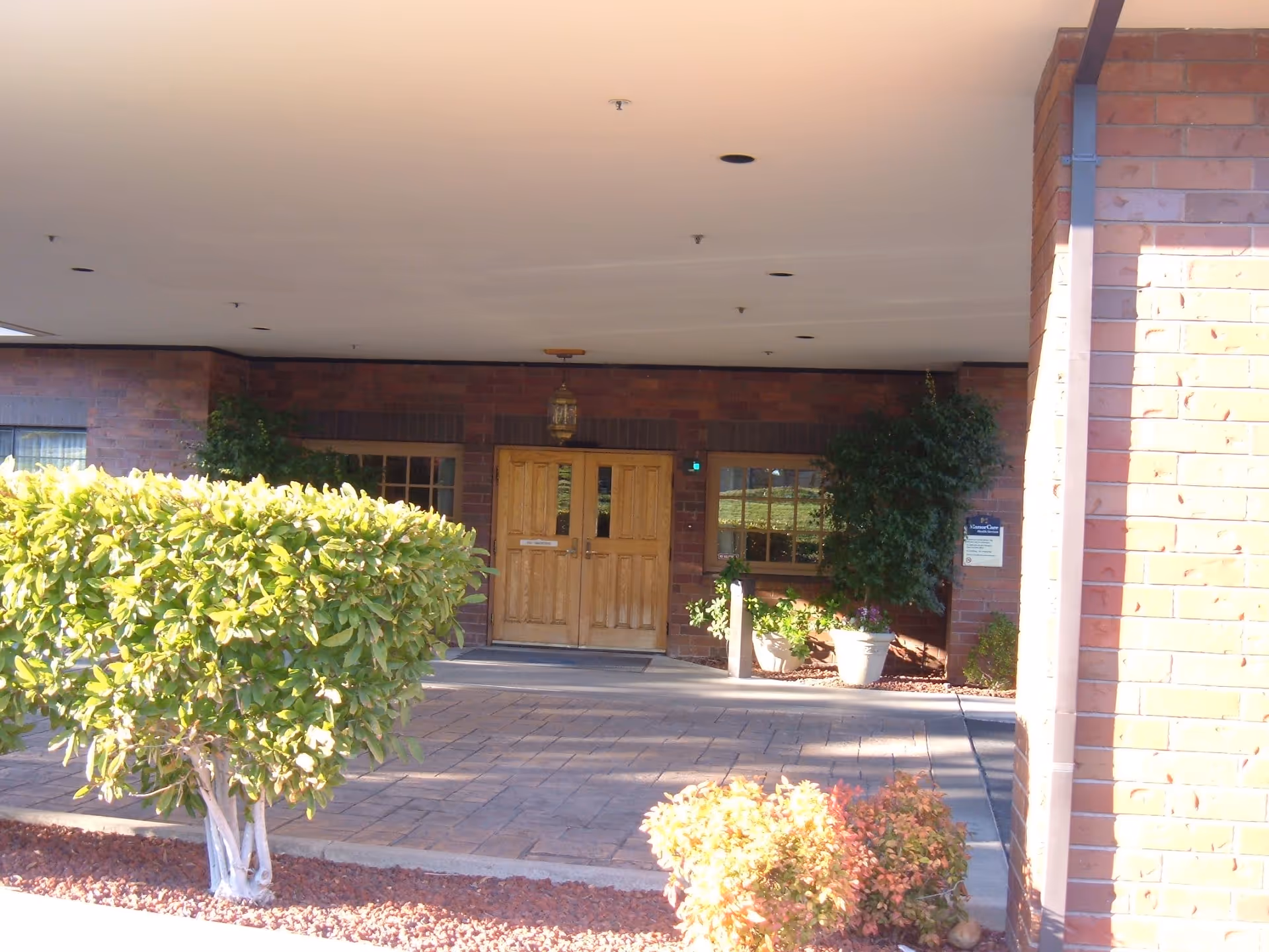 Bricked building entrance with wooden double doors under a covered drop-off area.