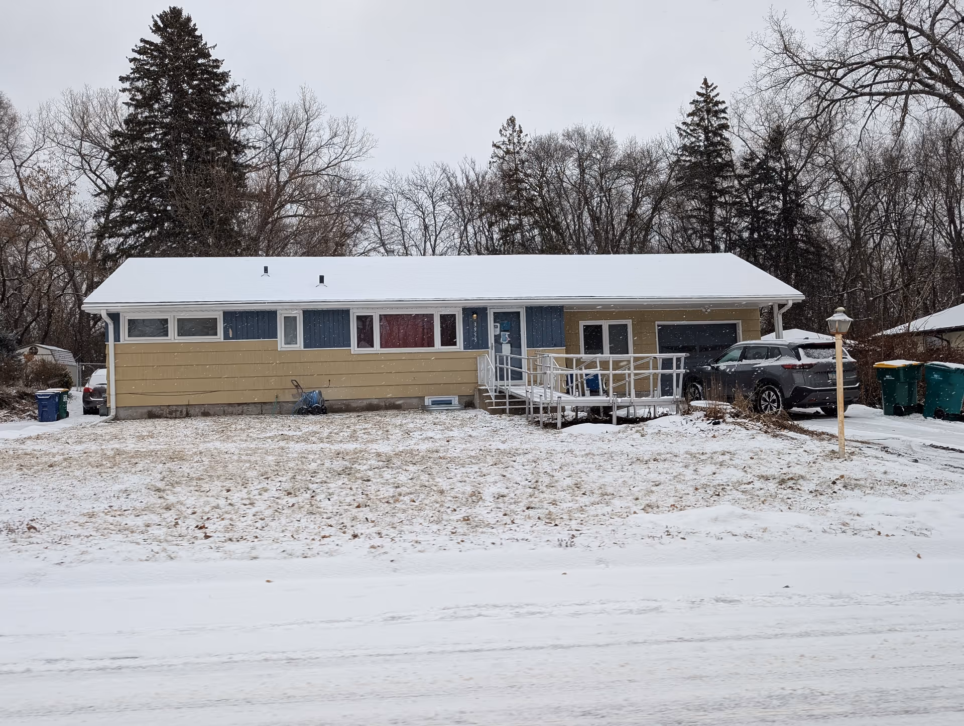 Single-story ranch-style house with a snowy front yard, a wheelchair ramp to the front door, and a parked car.