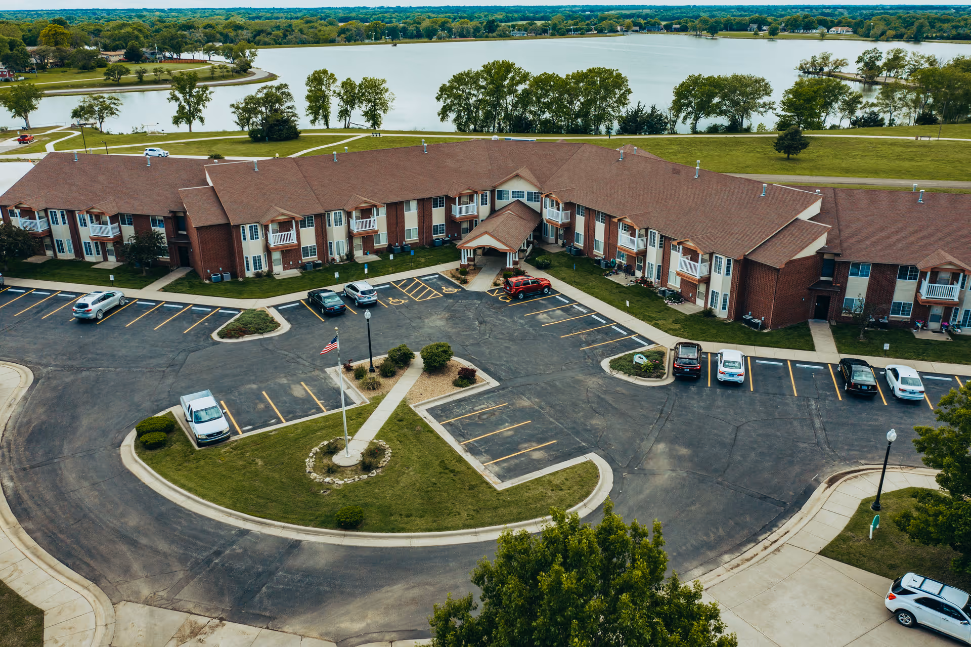 Aerial view of Cottonwood Point showing a U-shaped brick senior living building, central parking lot and landscaping with a lake in the background.