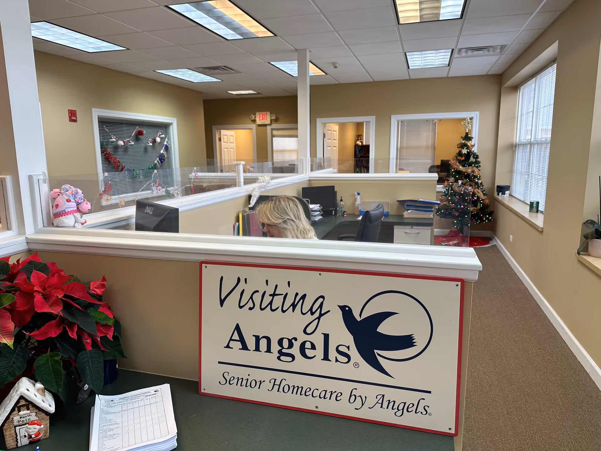Reception area with Visiting Angels sign, cubicles, holiday tree, and beige walls.