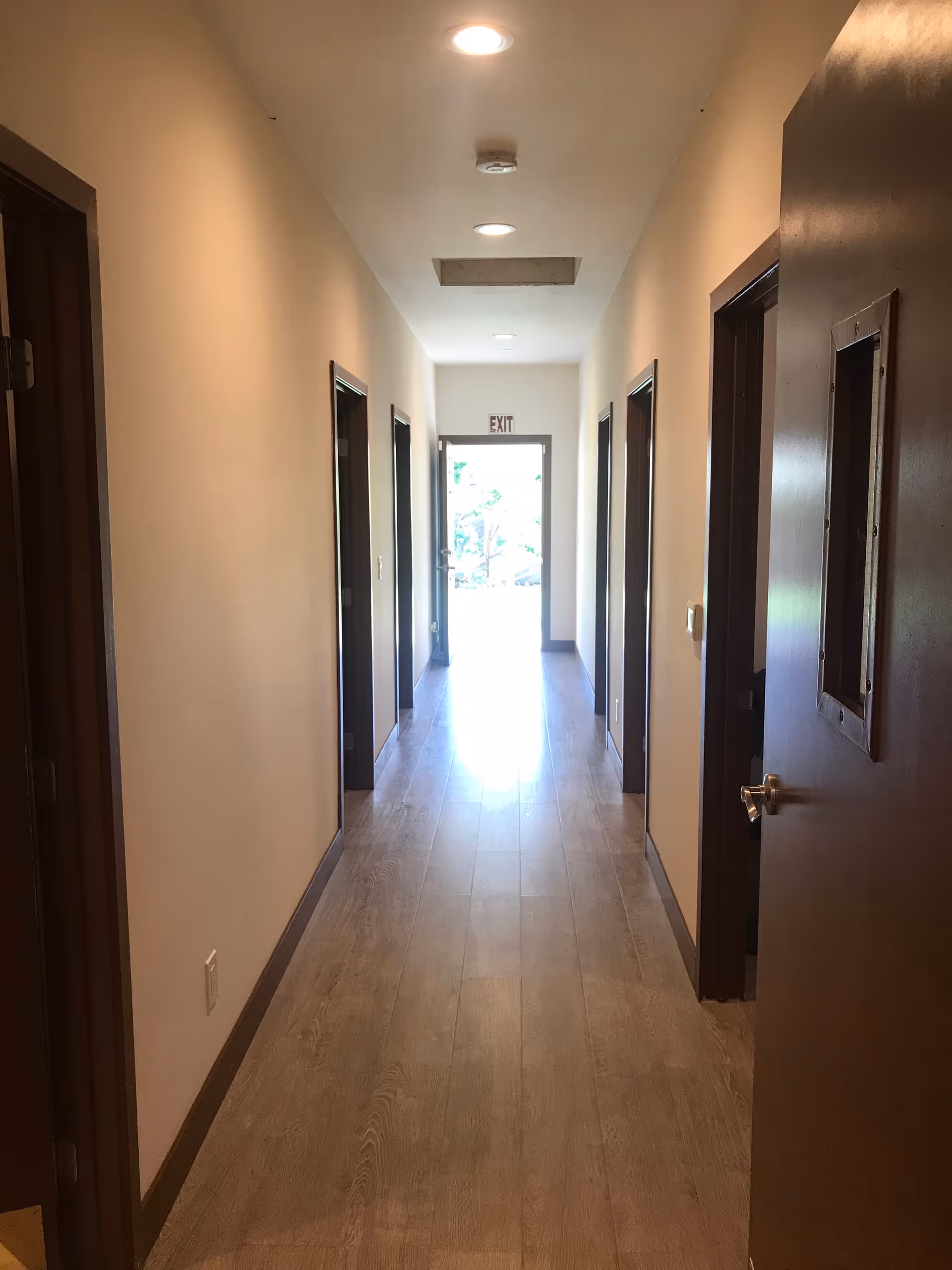 Long hallway in a senior living facility with closed doors and an exit at the end.