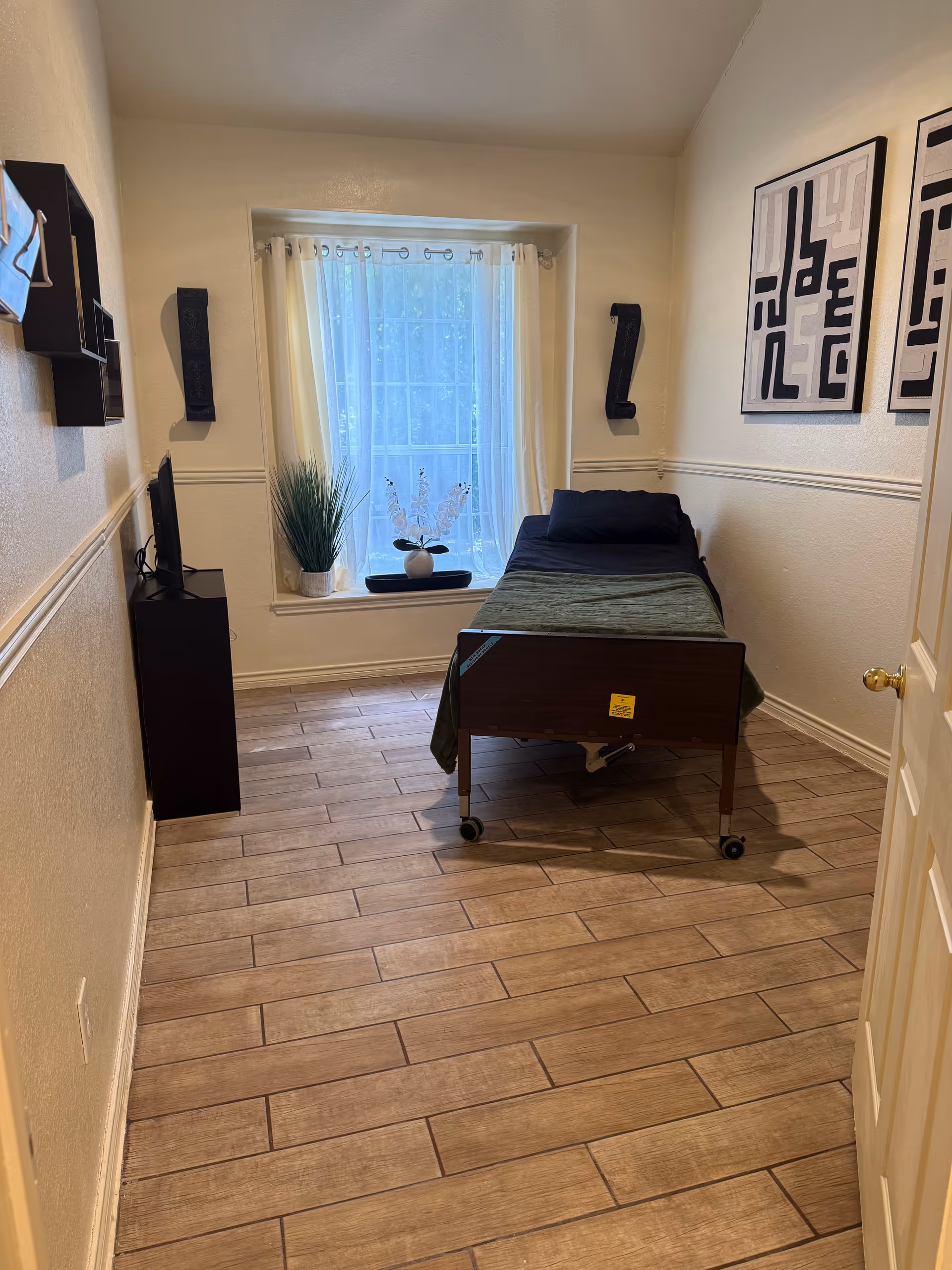 A small hospital-style bedroom with a single bed by a window and simple decor.