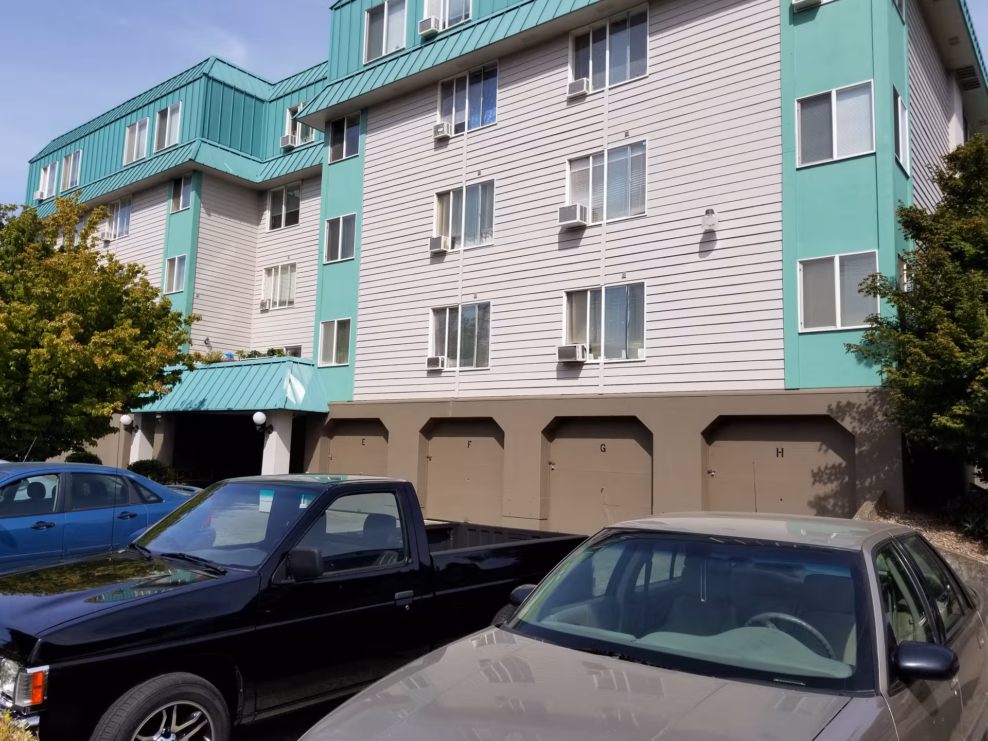 Multi-story senior living building with teal accents and parked cars in front.