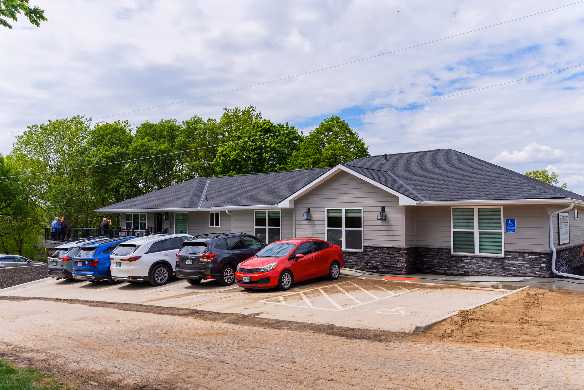 Single-story senior living building with parking lot and leafy backdrop.