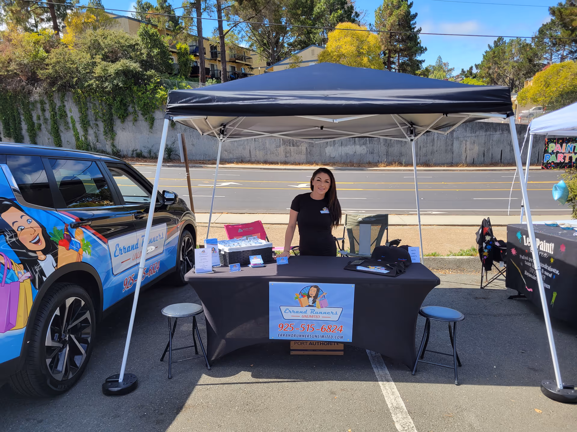 Smiling staff stands at an outdoor booth beside a branded Errand Runners Unlimited van.