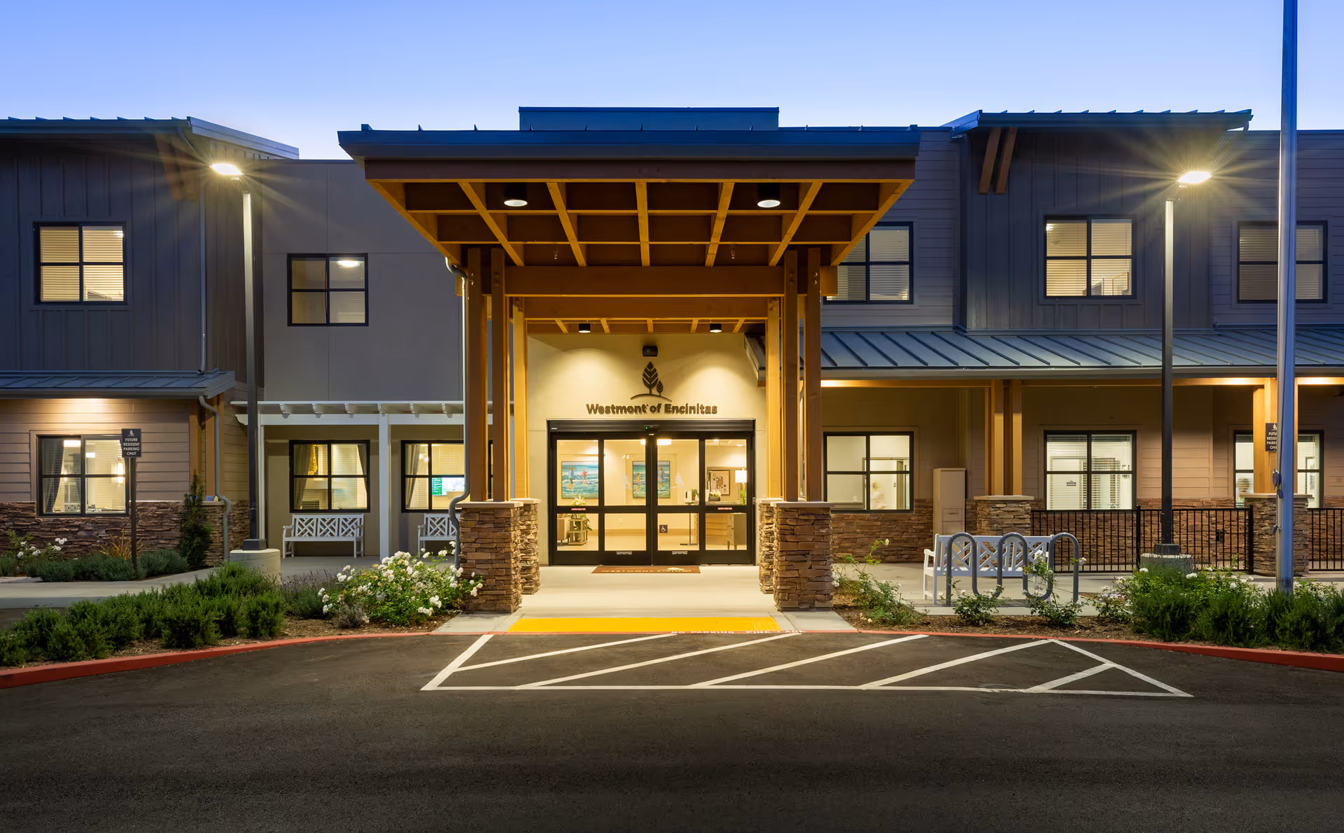 Evening exterior view of Westmont of Encinitas entrance with covered canopy and parking.