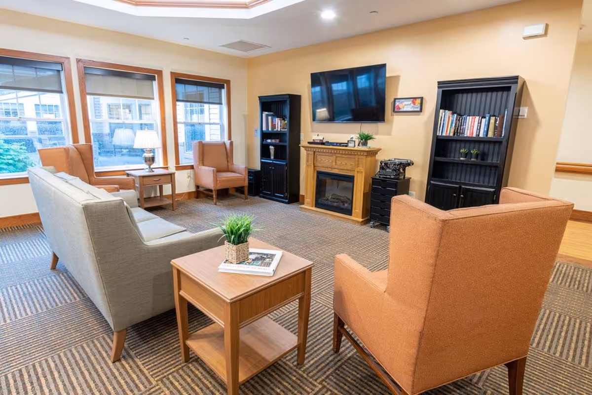 Cozy lounge with sofas, chairs, a fireplace, bookshelves, a TV, and large windows.