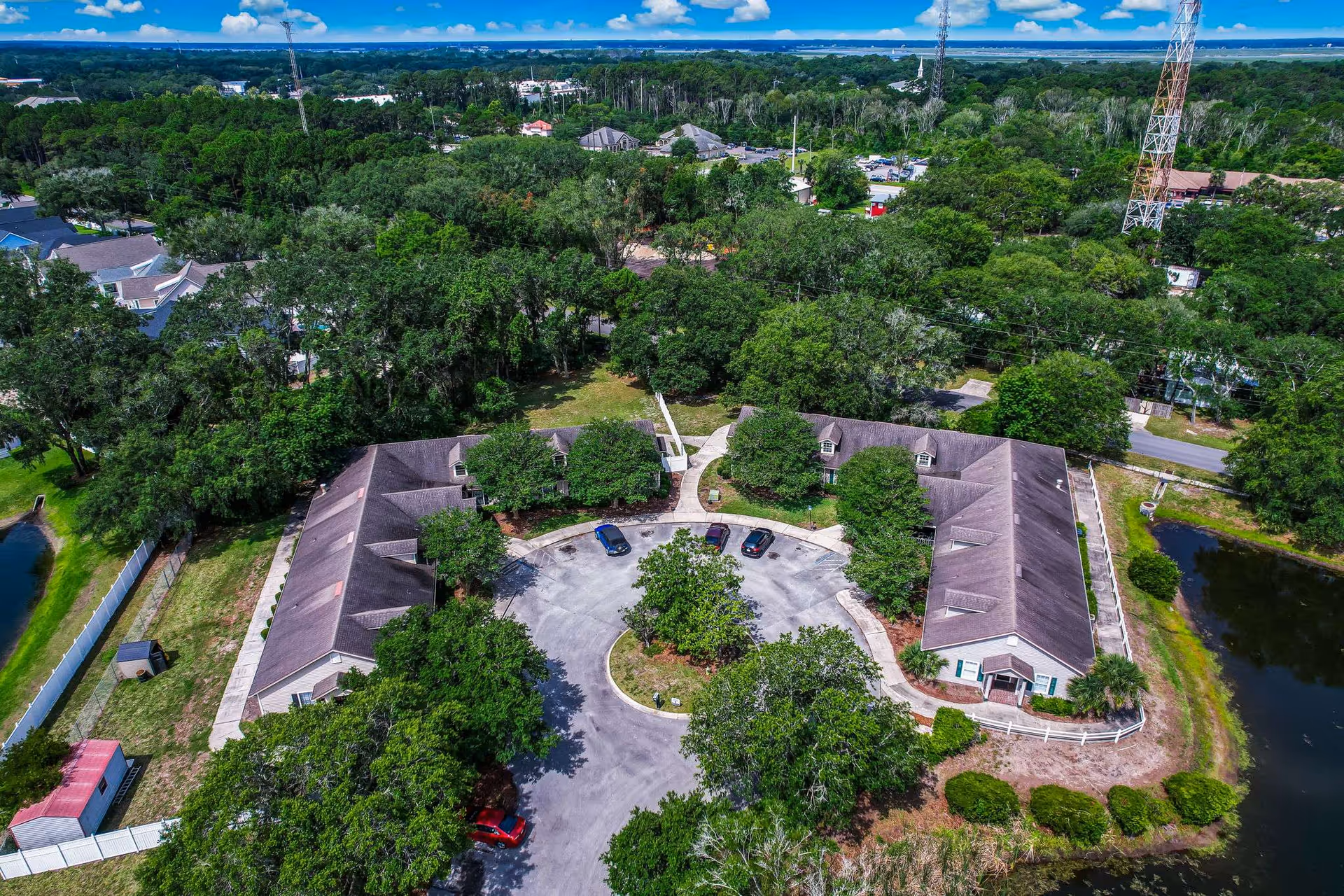 Aerial view of a horseshoe-shaped senior living campus with parking, trees, and a pond.