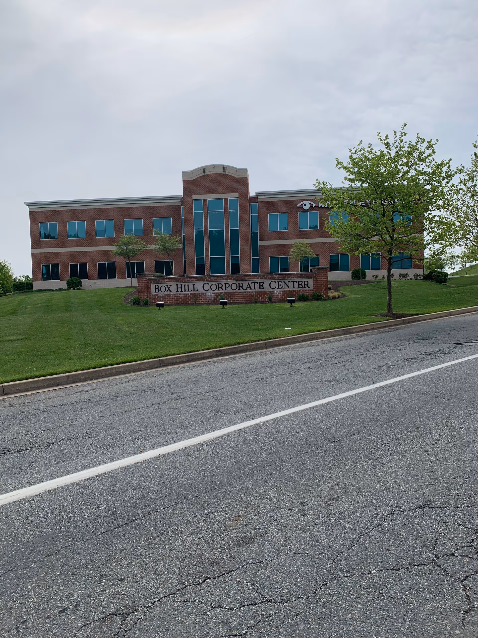Exterior view of a brick corporate center with a sign, trees, and a sloped lawn.