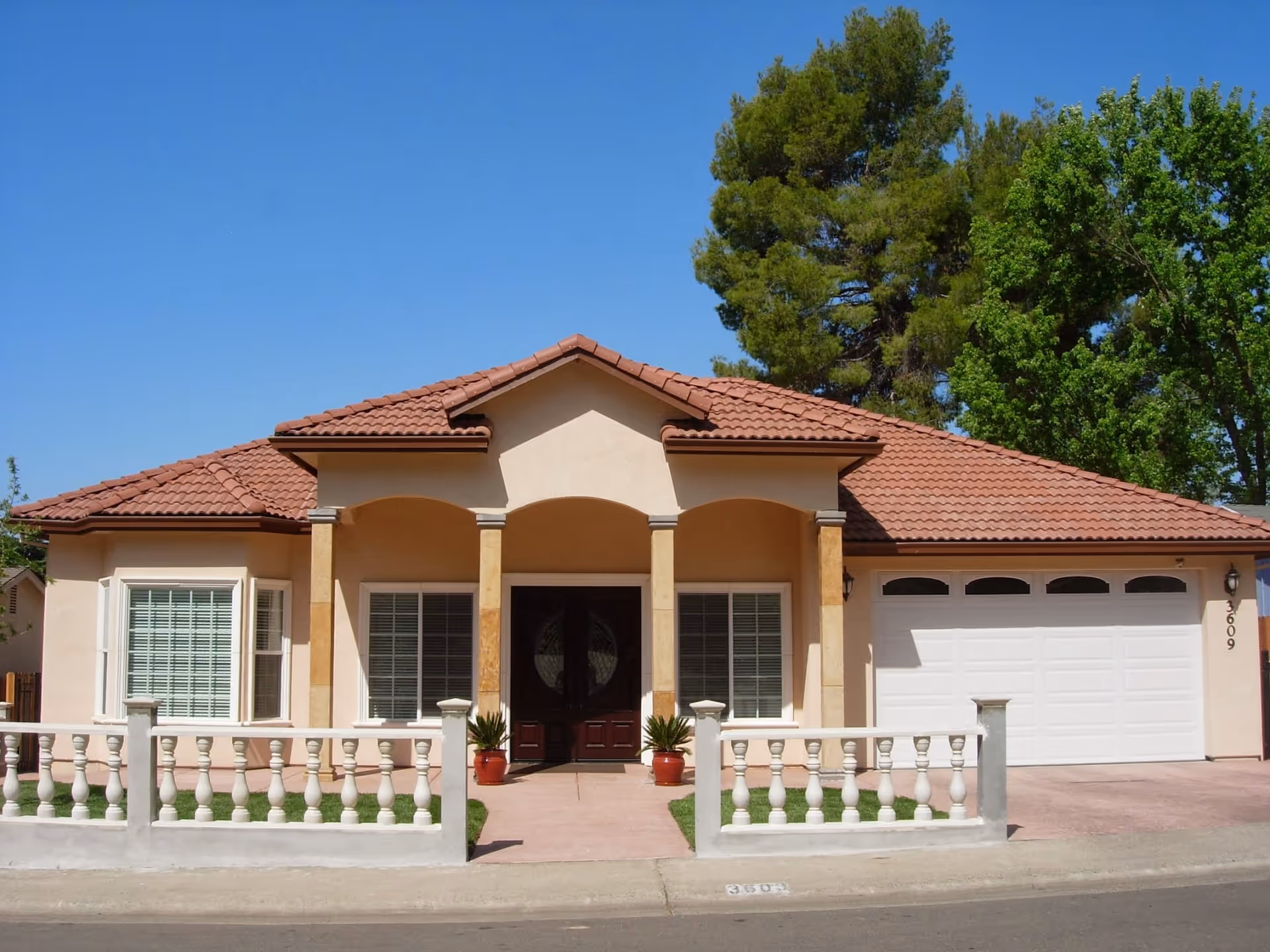 Front view of a beige stucco home with red tile roof, columns, and white railing.