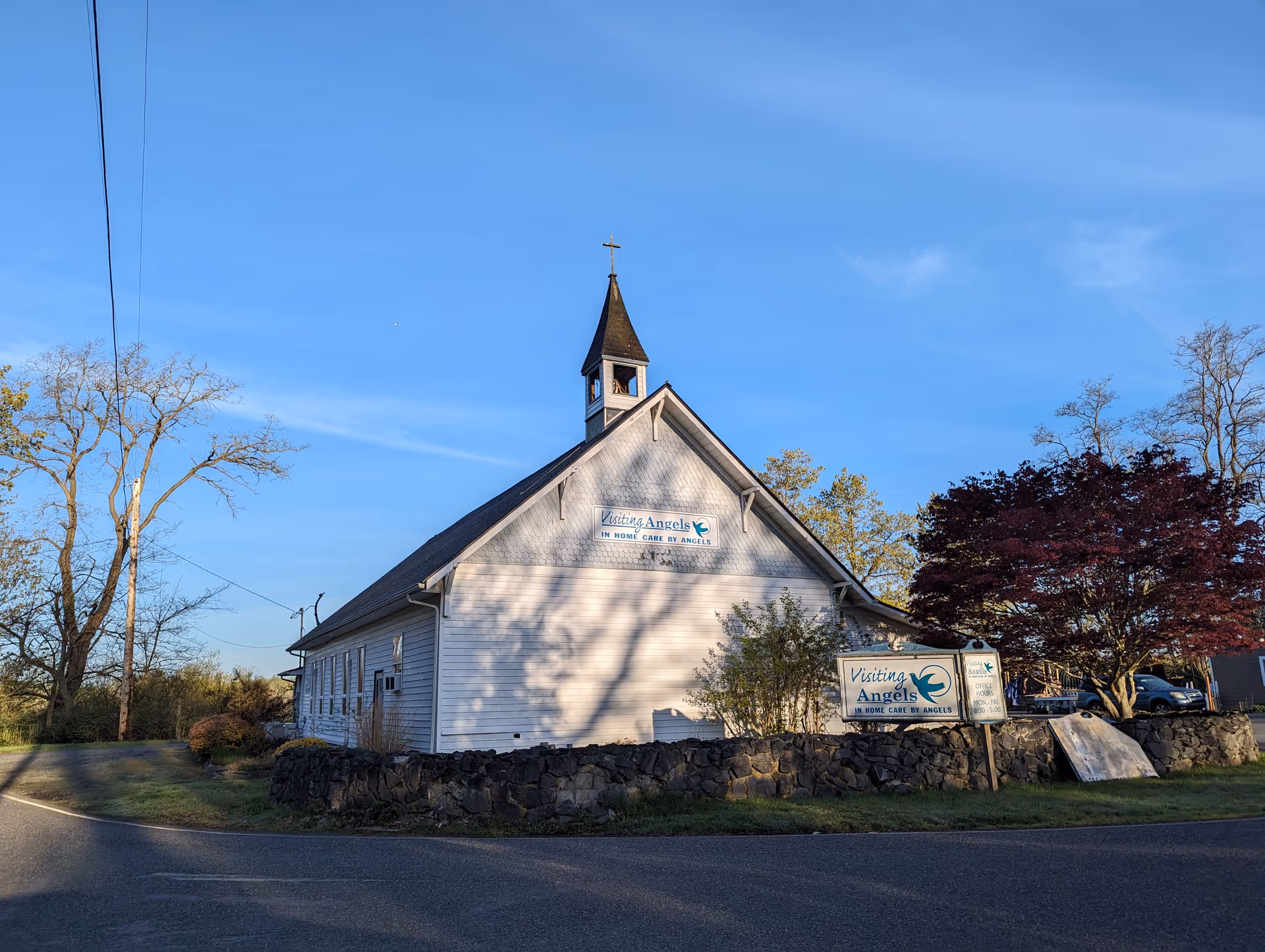 A small white building with a steeple and Visiting Angels sign in front.