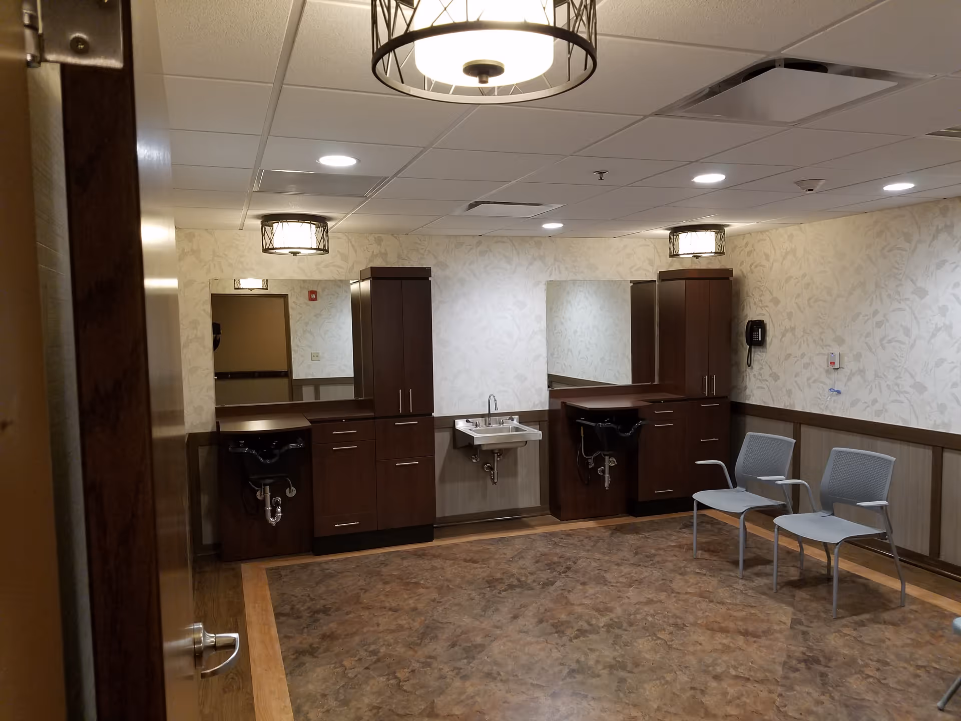 Salon area with mirrors, dark wood cabinets, two sinks, and chairs inside a senior living facility.