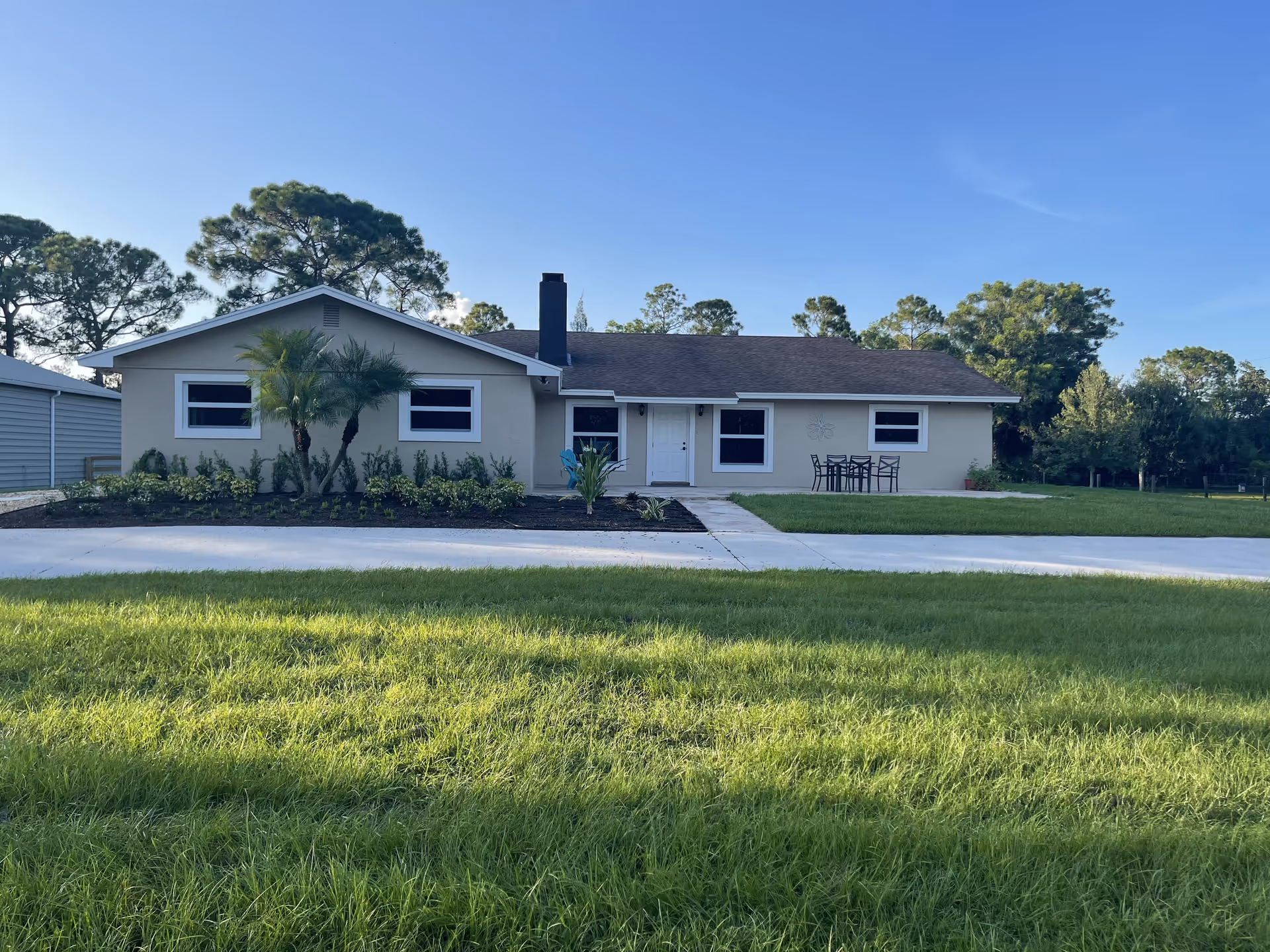 A single-story beige building with a front yard, palm tree, and outdoor table on the lawn.