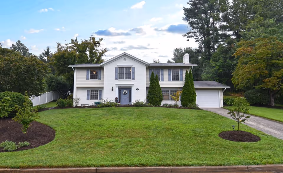 White two-story building with a manicured front lawn, shrubs, and an attached garage.