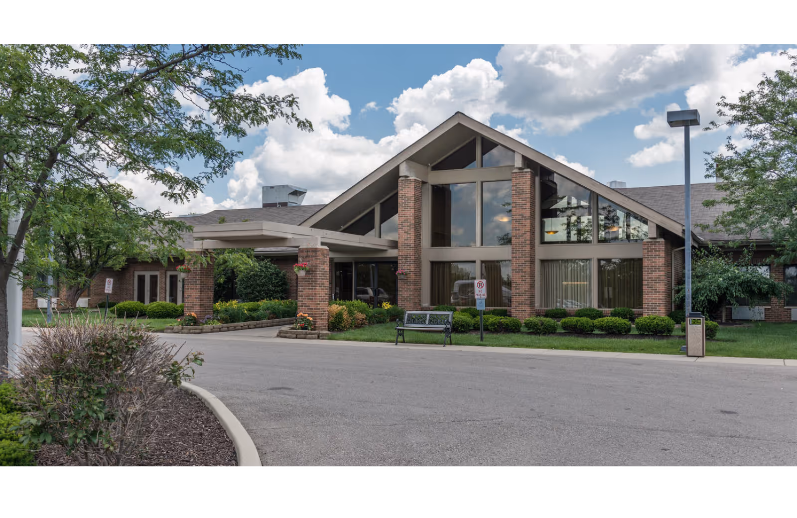 Gabled glass-front entrance of Legacy Miamisburg senior living facility with brick facade.