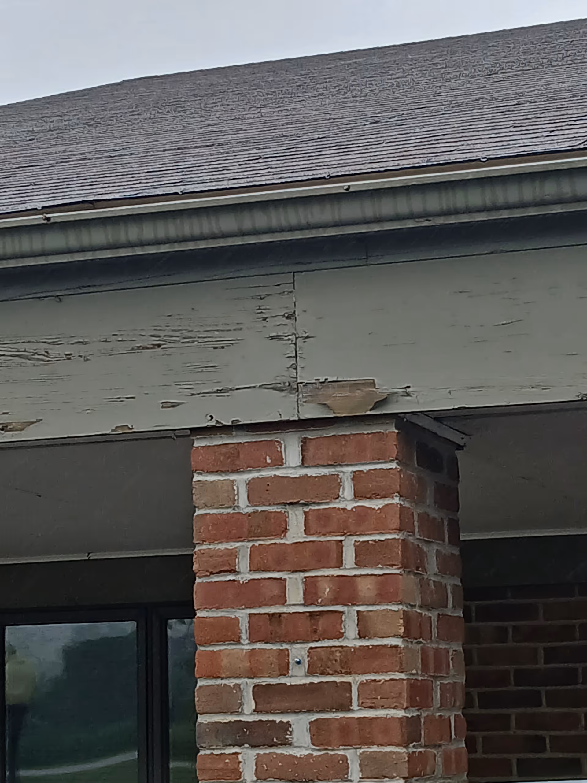 Exterior view of a brick column and peeling painted siding on the building facade.