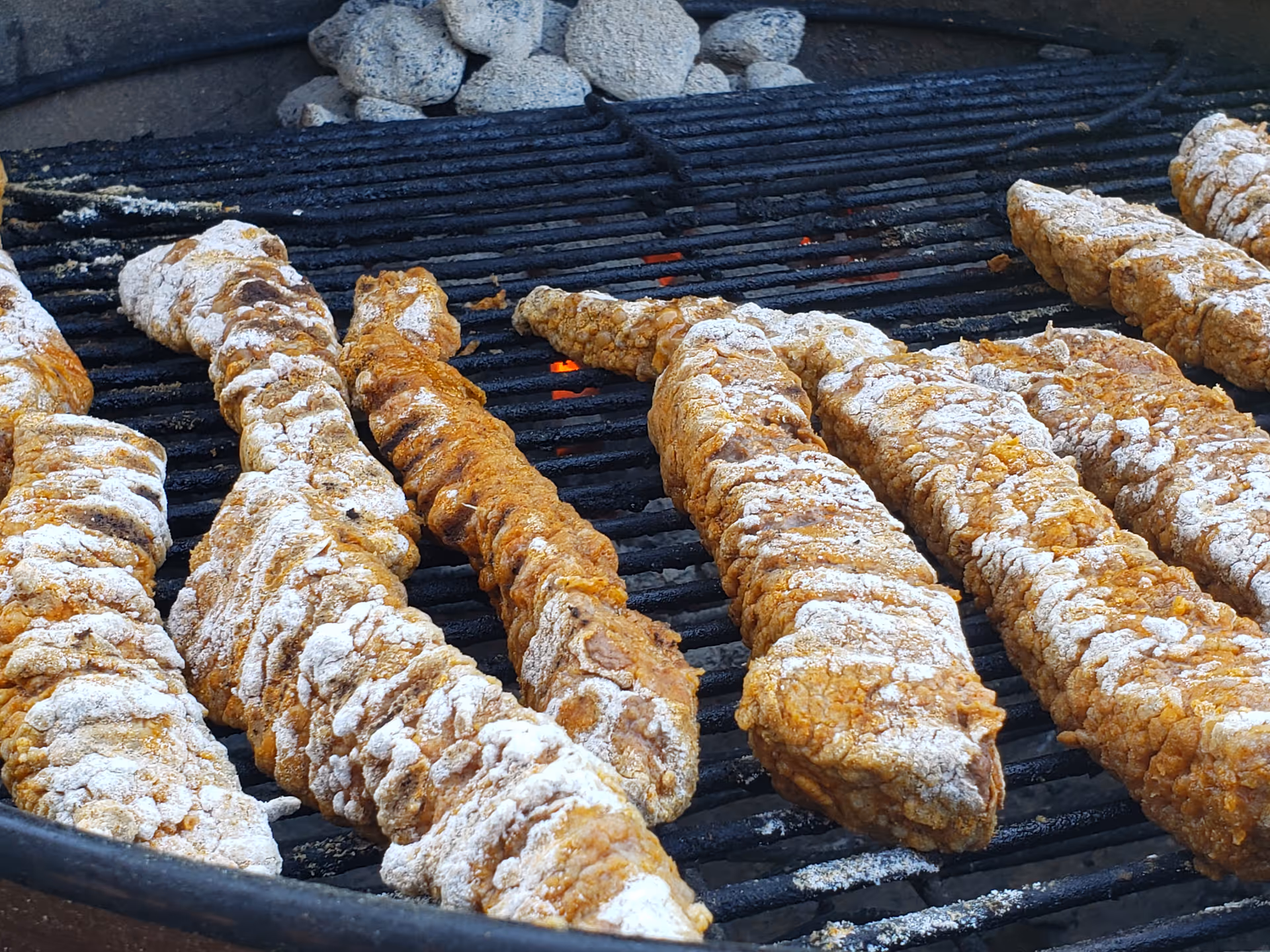 Long breaded sticks grilling on a charcoal outdoor barbecue.