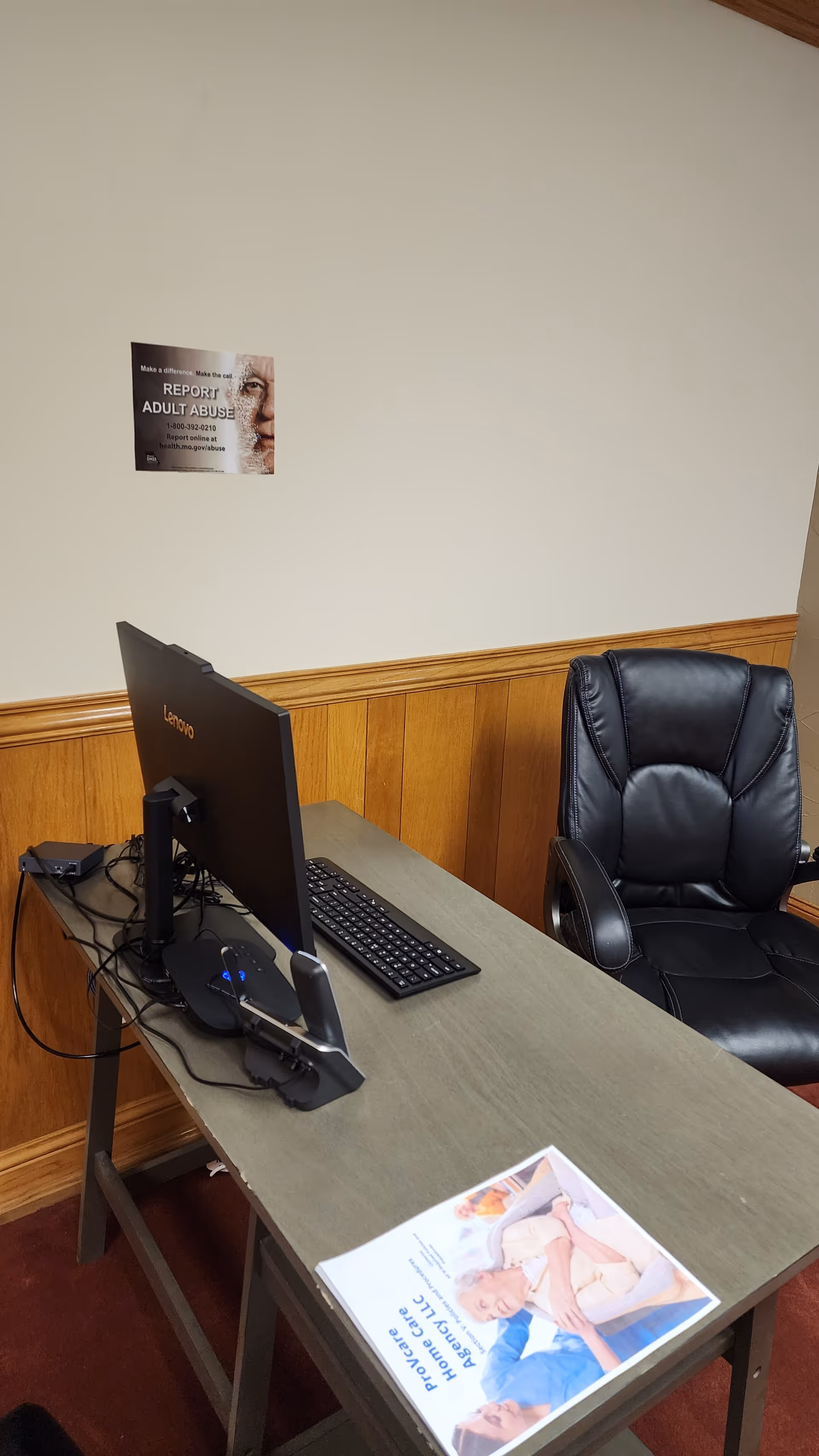 Office desk with computer and leather chair in wood-paneled room.