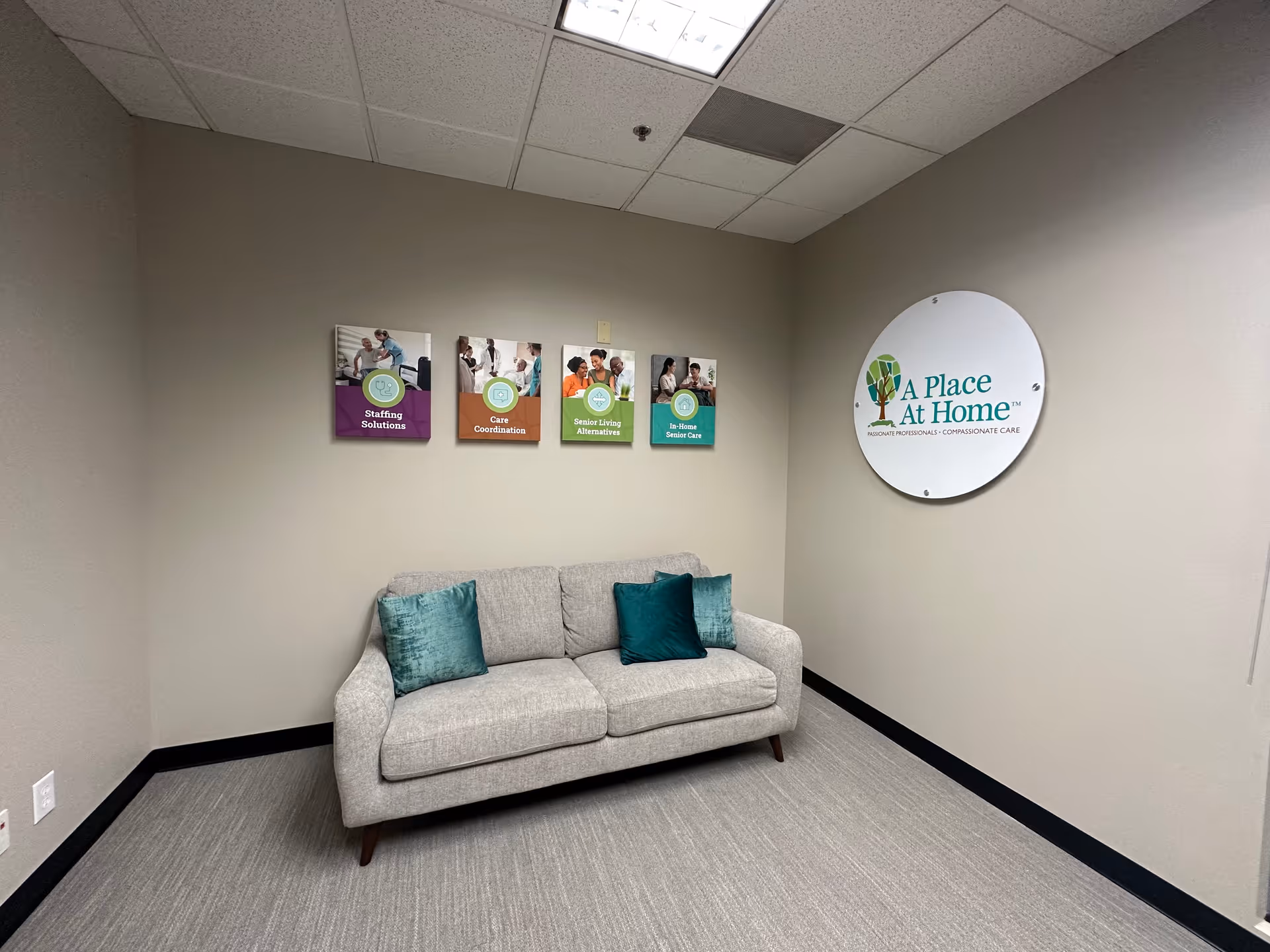 Cozy waiting area with gray sofa, teal pillows, wall brochures, and a Place At Home sign.