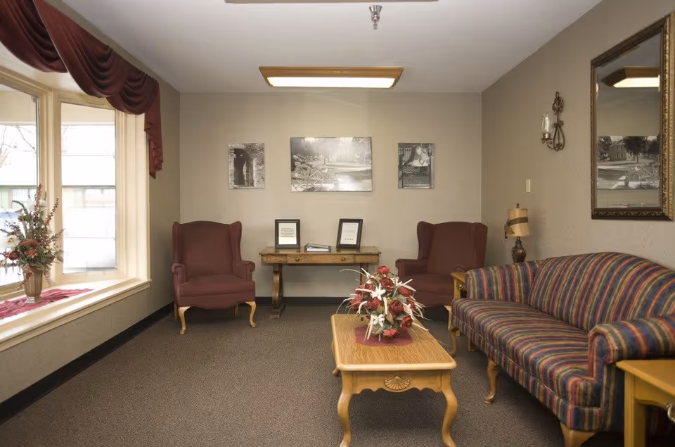 Cozy living room with two maroon armchairs, striped sofa, coffee table, and wall photos.