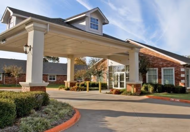 Senior living facility covered entrance with brick building, columns, and landscaped driveway.